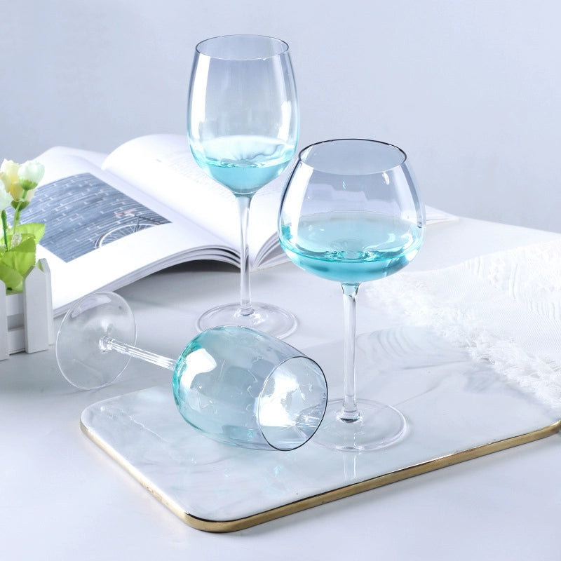 A collection of iridescent glassware from Domus Forge, featuring wine glasses, champagne coupes, decanters, and highball glasses in pastel gradient hues.