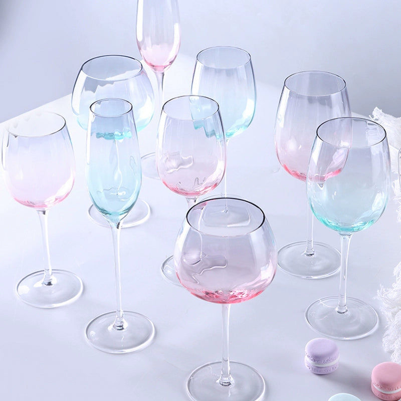 A collection of iridescent glassware from Domus Forge, featuring wine glasses, champagne coupes, decanters, and highball glasses in pastel gradient hues.