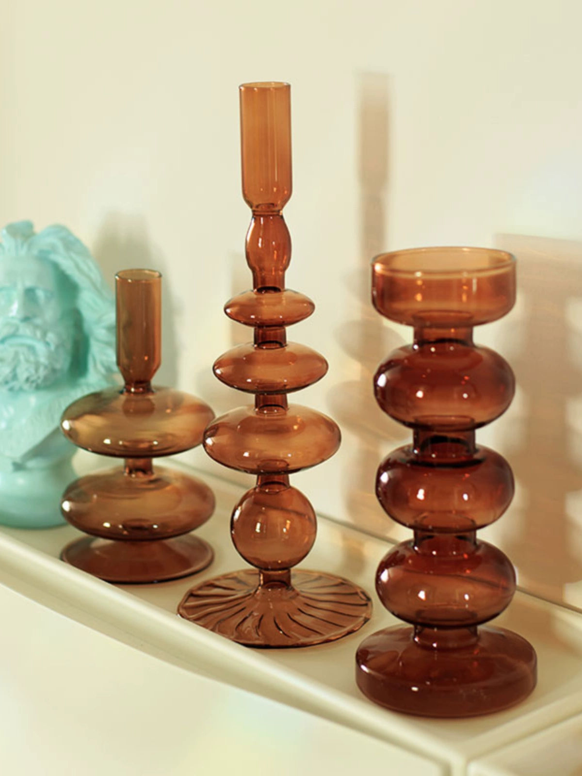 A brown glass Rhea Candle Holder set, featuring four different silhouettes in various sizes, creating a warm and inviting retro ambiance.