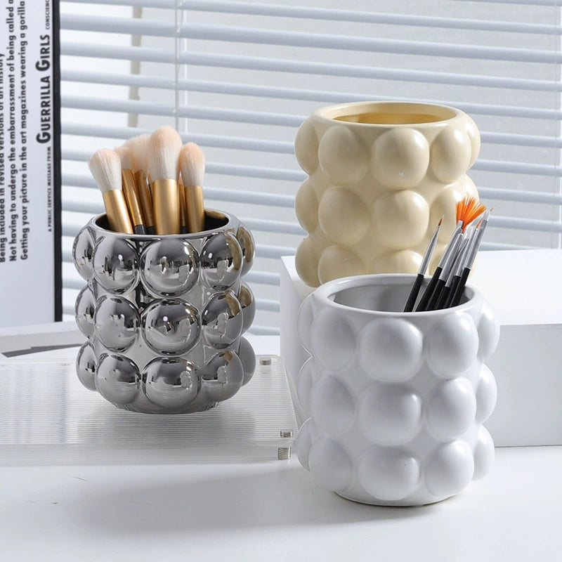 Image of the Vermi Beauty Jar, a ceramic vanity organizer with large beaded details, available in three colorways: white, milk, or silver. This stylish, modern jar is designed for organizing cosmetic brushes and beauty products on a bathroom countertop, ideal for home décor enthusiasts.