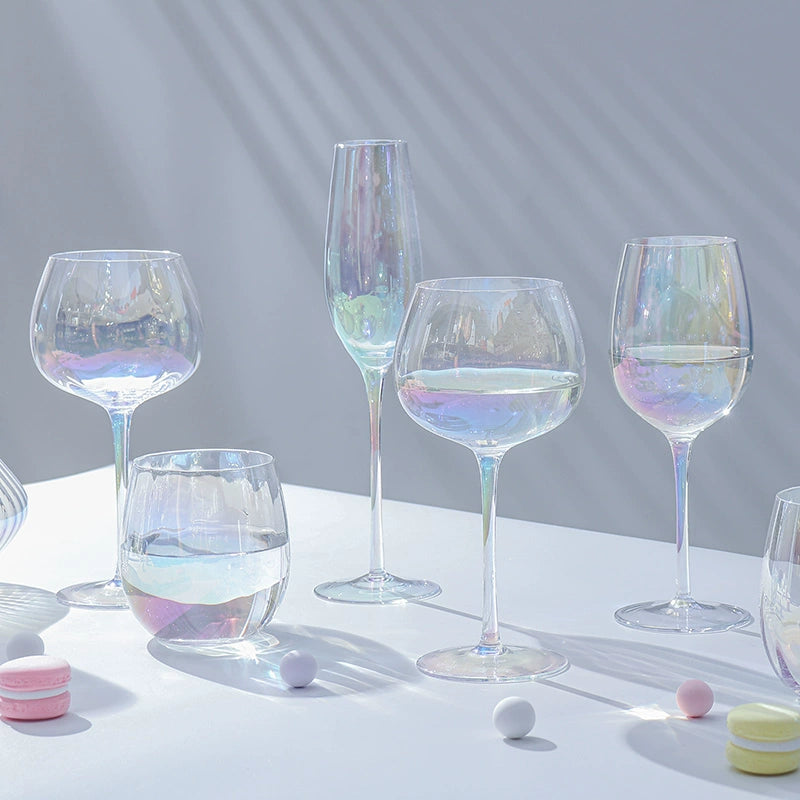 A collection of iridescent glassware from Domus Forge, featuring wine glasses, champagne coupes, decanters, and highball glasses in pastel gradient hues.