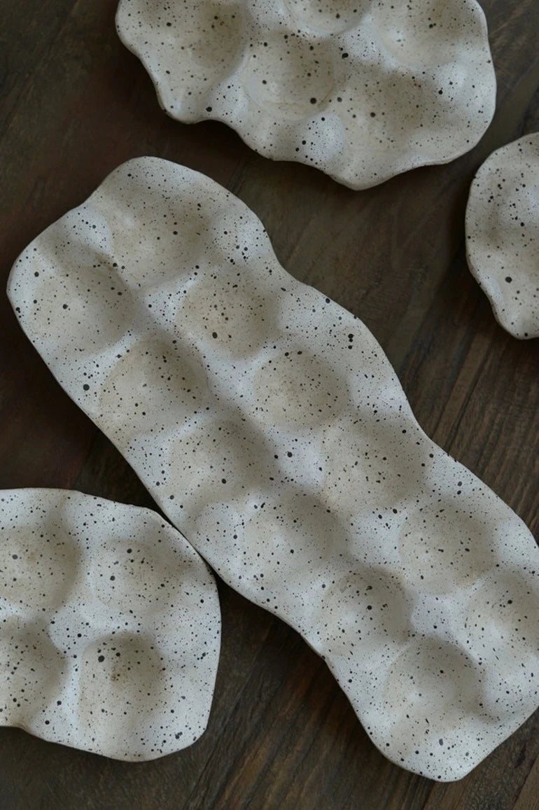 A ceramic Umiko Egg Crate featuring an organic shape, ivory finish with black paint splatters, available in half a dozen or a dozen slots, adding uniqueness to kitchen décor.