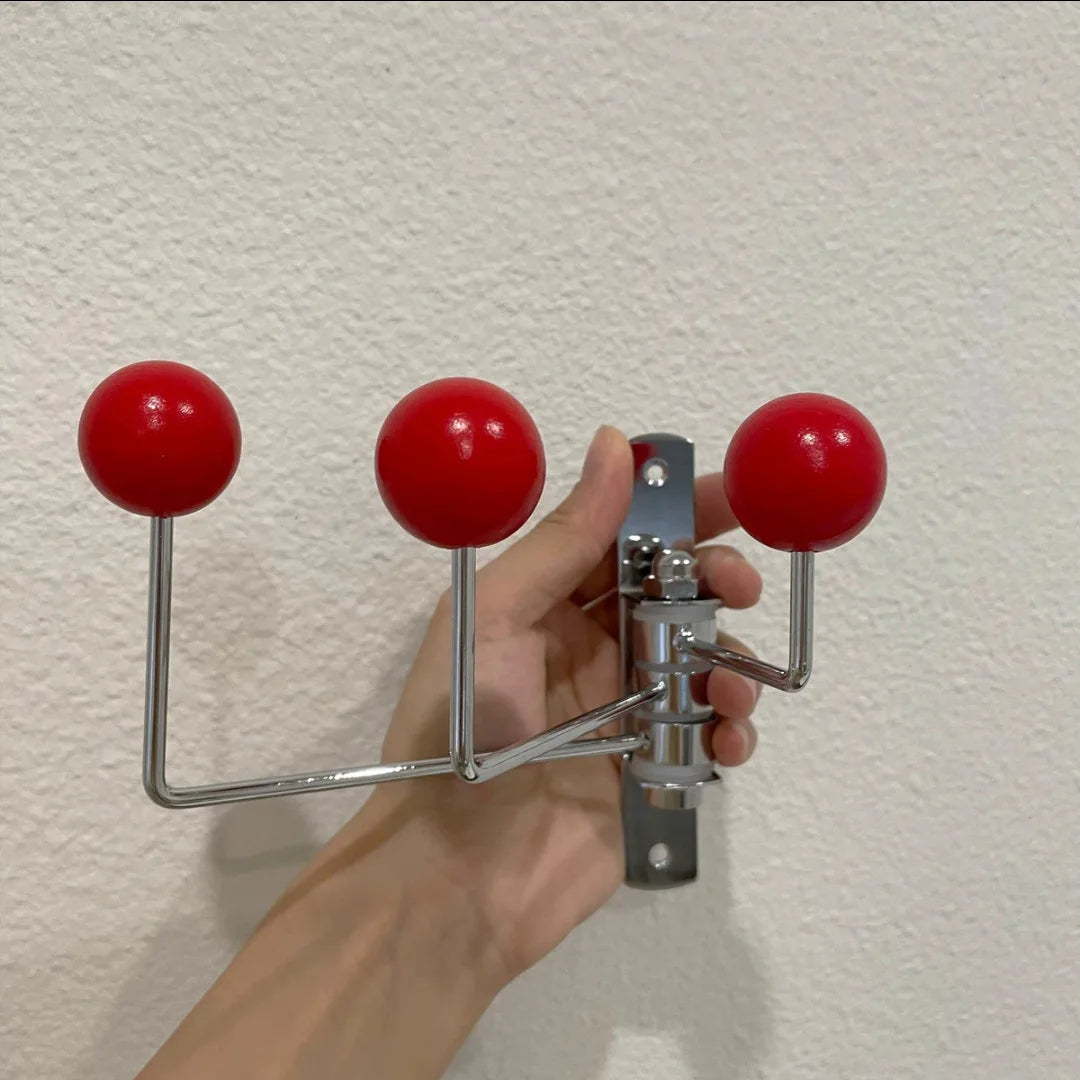 A silver wall-mounted rack with three hooks, each featuring bright wooden ball accents. The Randi Wall Rack has a modern yet vintage-inspired design, ideal for hanging towels or accessories in entryways, bathrooms, or bedrooms. Perfect for home decor enthusiasts seeking a stylish, space-saving storage solution.