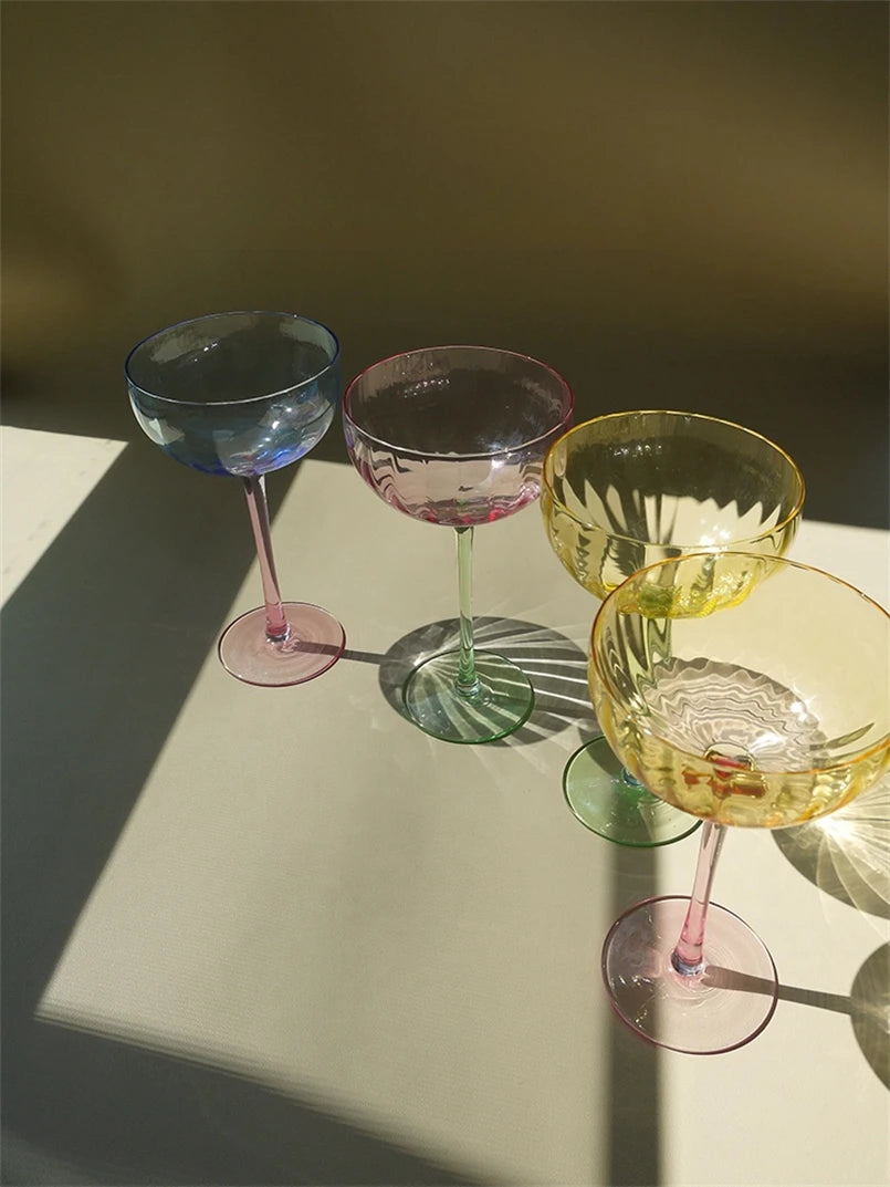A vibrant collection of Ugo Wine Glasses displayed on a table, showcasing their fun and chic design. Each glass features a colored pastel bowl with a contrasting stem and a fluted shape. Ideal for entertaining, these glasses hold 11 fluid ounces and are perfect for mixing and matching. Designed for home décor enthusiasts, they add a playful yet elegant touch to any bar or dining setting.