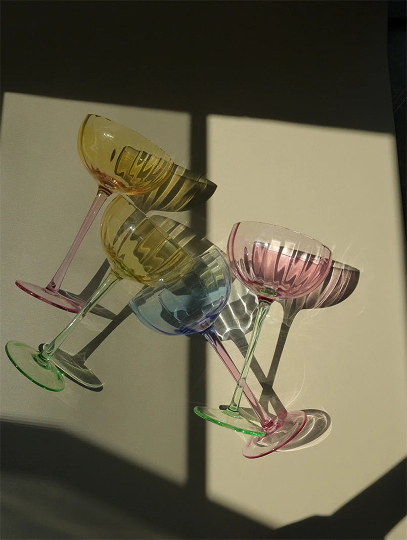 A vibrant collection of Ugo Wine Glasses displayed on a table, showcasing their fun and chic design. Each glass features a colored pastel bowl with a contrasting stem and a fluted shape. Ideal for entertaining, these glasses hold 11 fluid ounces and are perfect for mixing and matching. Designed for home décor enthusiasts, they add a playful yet elegant touch to any bar or dining setting.