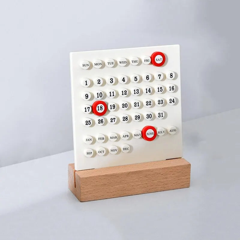 Image of the Callie Calendar, a compact, reusable calendar in black or white with a sleek acrylic design and a natural wooden stand. Features a red marker for highlighting important dates, perfect for organizing spaces like the kitchen or office with a touch of style.
