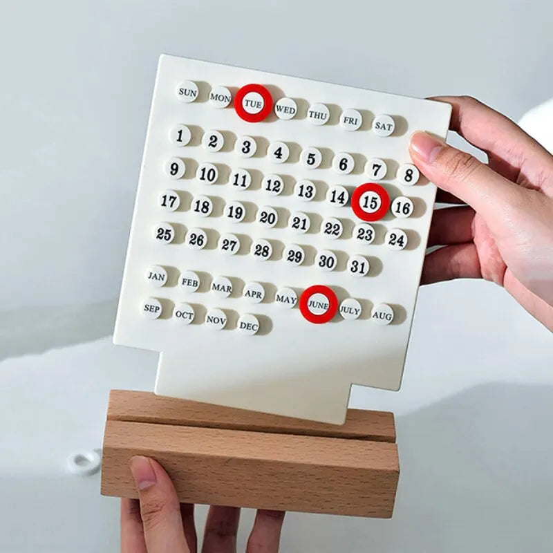 Image of the Callie Calendar, a compact, reusable calendar in black or white with a sleek acrylic design and a natural wooden stand. Features a red marker for highlighting important dates, perfect for organizing spaces like the kitchen or office with a touch of style.