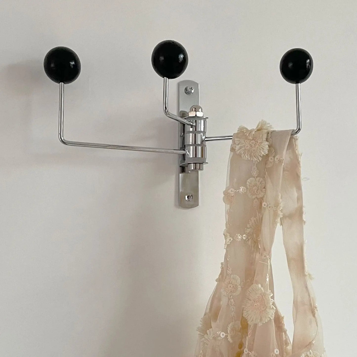 A silver wall-mounted rack with three hooks, each featuring bright wooden ball accents. The Randi Wall Rack has a modern yet vintage-inspired design, ideal for hanging towels or accessories in entryways, bathrooms, or bedrooms. Perfect for home decor enthusiasts seeking a stylish, space-saving storage solution.