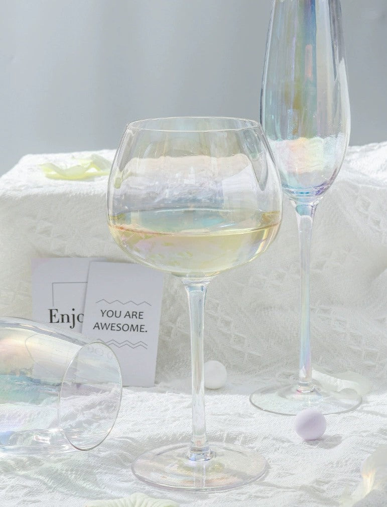 A collection of iridescent glassware from Domus Forge, featuring wine glasses, champagne coupes, decanters, and highball glasses in pastel gradient hues.