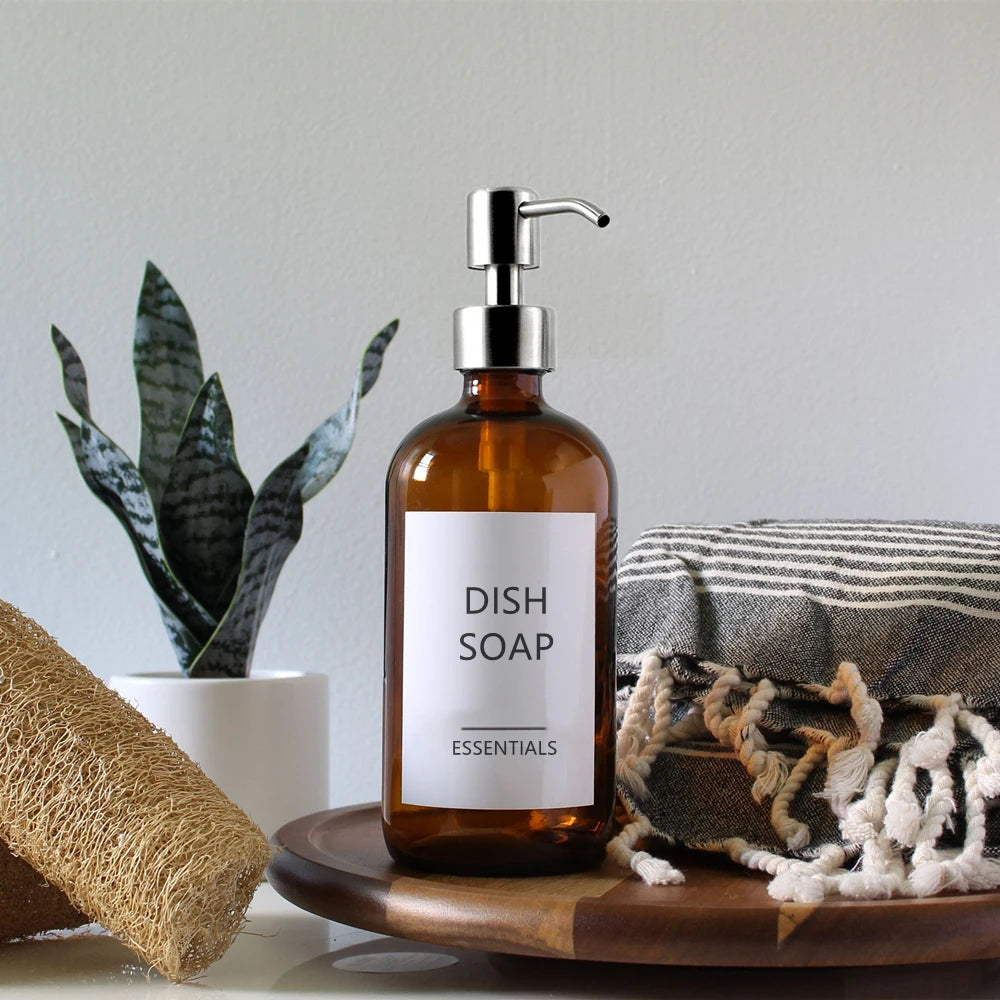 A set of two amber glass soap dispensers, each with a 16 oz capacity, featuring a choice of silver or black stainless steel pumps. Includes six printed labels for easy identification. Ideal for home décor enthusiasts, this reusable and refillable set adds a stylish touch to kitchens and bathrooms.
