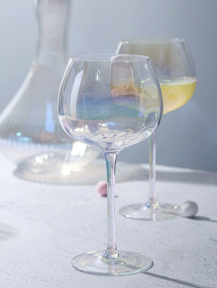 A collection of iridescent glassware from Domus Forge, featuring wine glasses, champagne coupes, decanters, and highball glasses in pastel gradient hues.