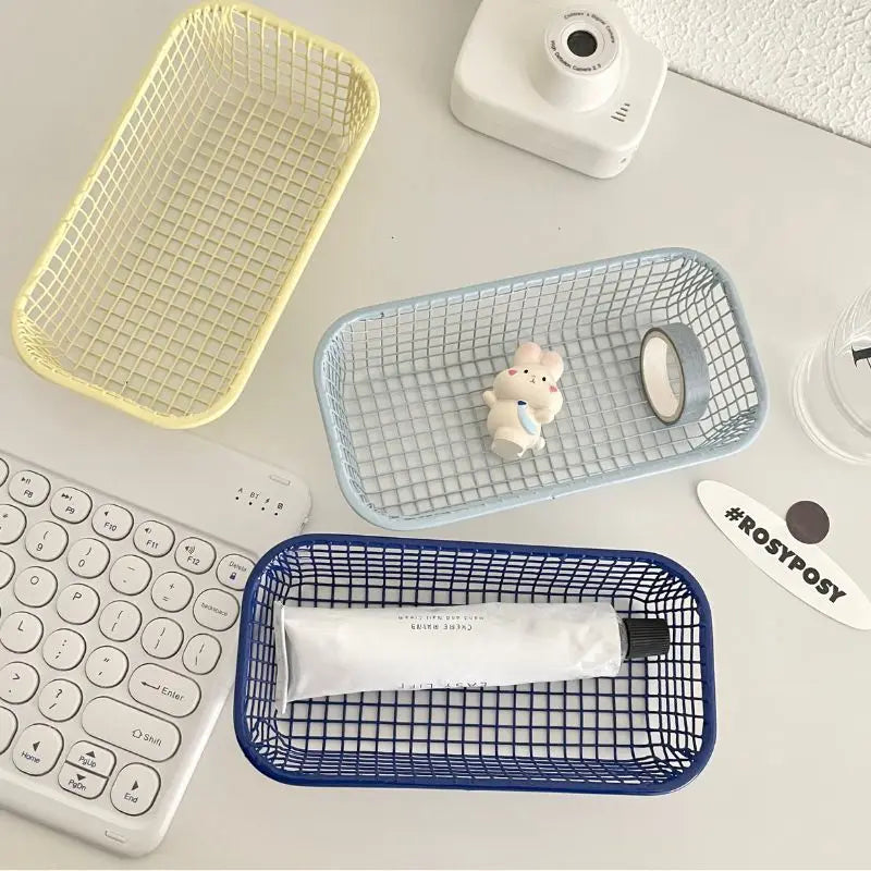 A small, versatile Elon Storage Basket displayed in a minimalist setting. The basket, made of durable metal, comes in butter yellow, sky blue, and navy. It is ideal for various uses, including organizing kitchen essentials, office supplies, or bath accessories. The sleek, utilitarian design complements modern and functional decor. The basket is shown in different color combinations, highlighting its mix-and-match capability for cohesive organization.