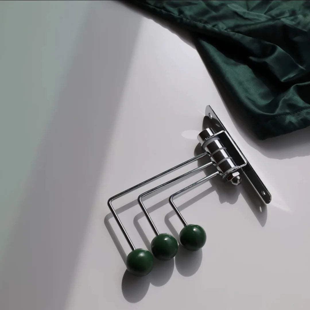 A silver wall-mounted rack with three hooks, each featuring bright wooden ball accents. The Randi Wall Rack has a modern yet vintage-inspired design, ideal for hanging towels or accessories in entryways, bathrooms, or bedrooms. Perfect for home decor enthusiasts seeking a stylish, space-saving storage solution.