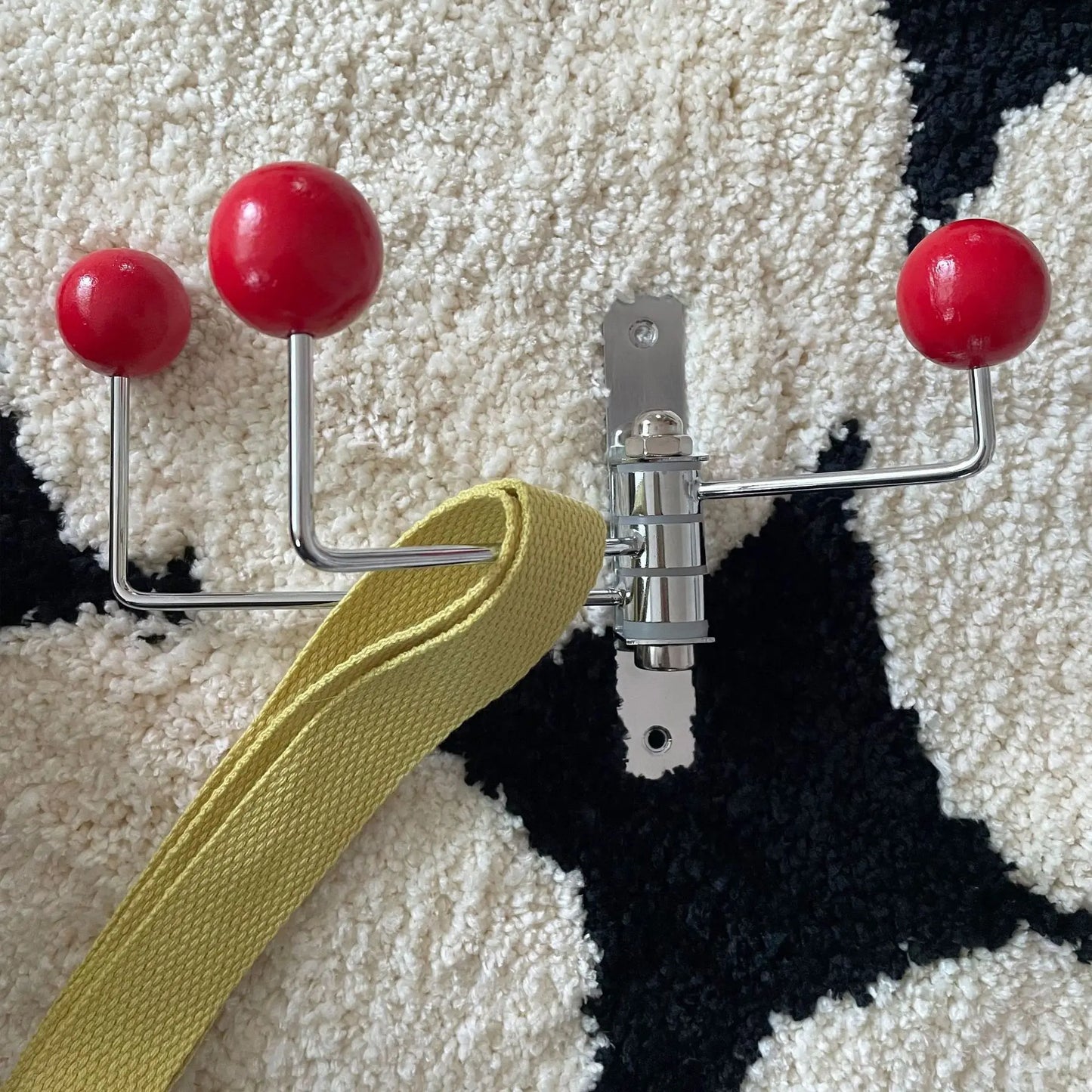 A silver wall-mounted rack with three hooks, each featuring bright wooden ball accents. The Randi Wall Rack has a modern yet vintage-inspired design, ideal for hanging towels or accessories in entryways, bathrooms, or bedrooms. Perfect for home decor enthusiasts seeking a stylish, space-saving storage solution.