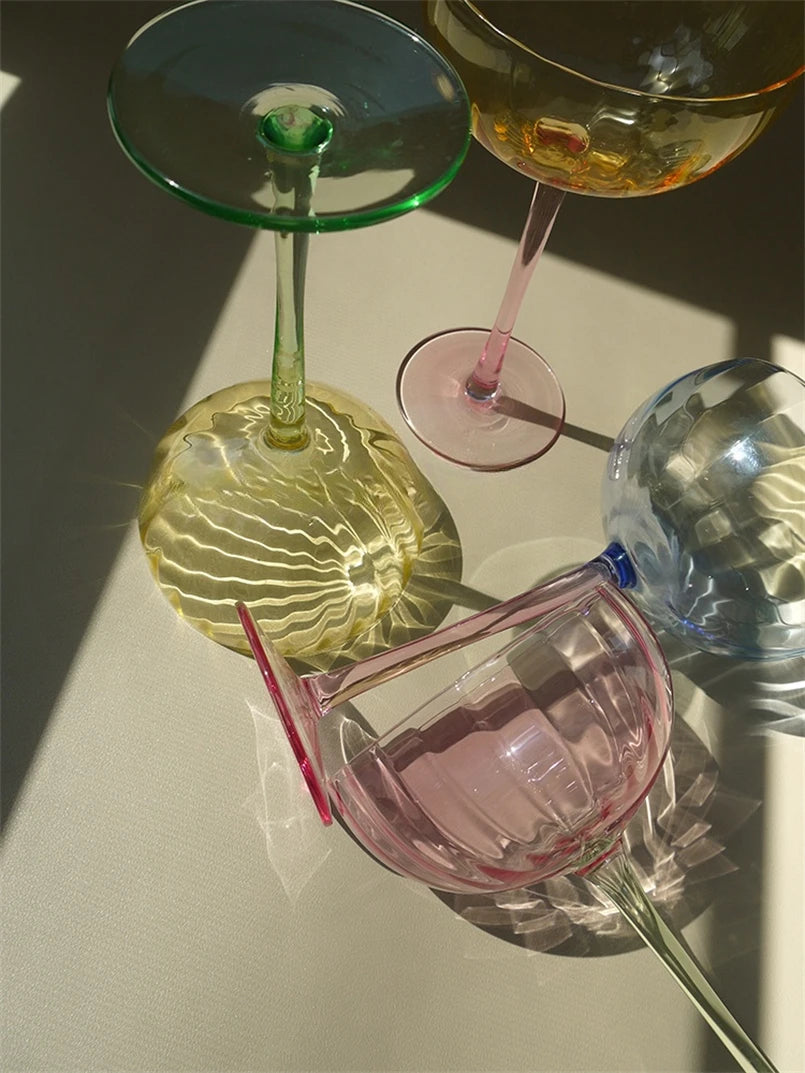 A vibrant collection of Ugo Wine Glasses displayed on a table, showcasing their fun and chic design. Each glass features a colored pastel bowl with a contrasting stem and a fluted shape. Ideal for entertaining, these glasses hold 11 fluid ounces and are perfect for mixing and matching. Designed for home décor enthusiasts, they add a playful yet elegant touch to any bar or dining setting.