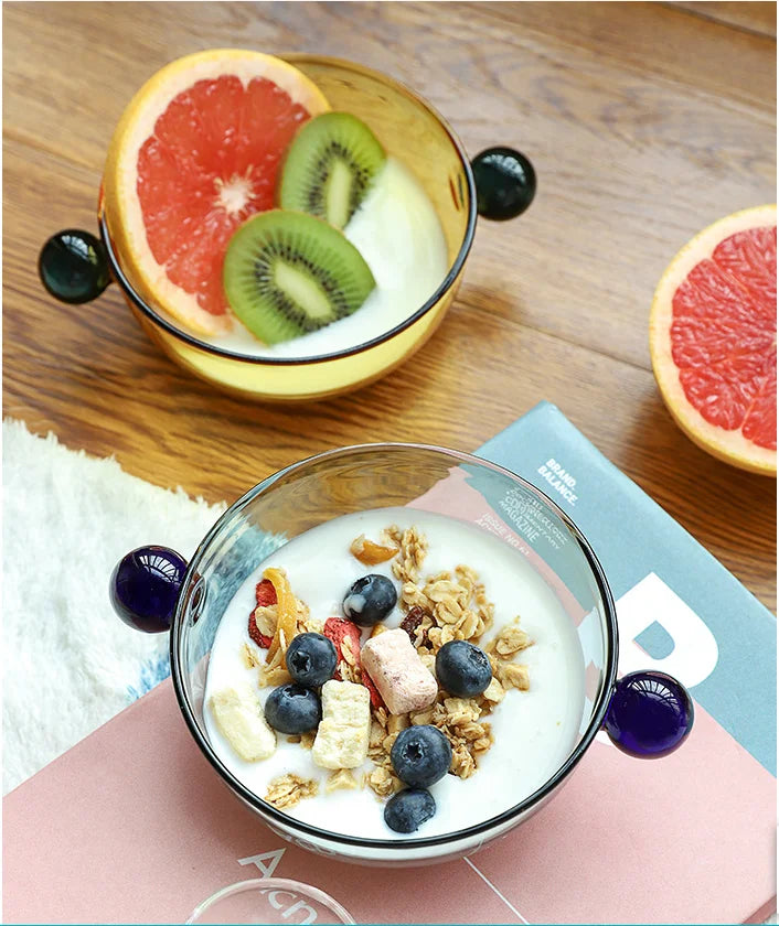 A stylish Xenos Serving Bowl made from borosilicate glass, measuring 11 cm in width with a depth of 4.5 cm. The bowl features glass knob handles and is available in various colorways. It is BPA-free, heat-resistant, and perfect for serving snacks, ice cream, cereal, or toppings. Ideal for home décor enthusiasts, this elegant bowl adds both functionality and charm to any kitchen setting.