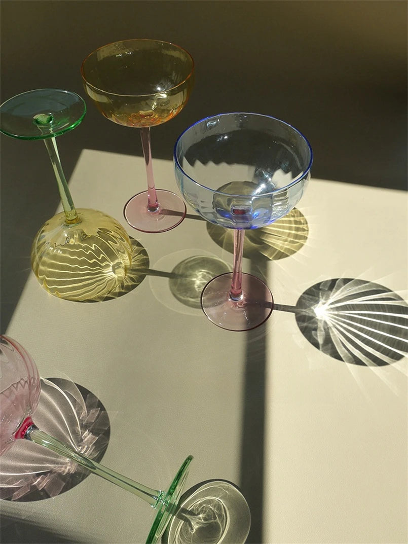 A vibrant collection of Ugo Wine Glasses displayed on a table, showcasing their fun and chic design. Each glass features a colored pastel bowl with a contrasting stem and a fluted shape. Ideal for entertaining, these glasses hold 11 fluid ounces and are perfect for mixing and matching. Designed for home décor enthusiasts, they add a playful yet elegant touch to any bar or dining setting.