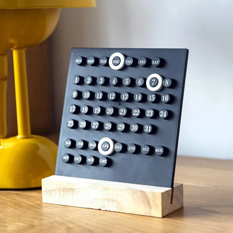 Image of the Callie Calendar, a compact, reusable calendar in black or white with a sleek acrylic design and a natural wooden stand. Features a red marker for highlighting important dates, perfect for organizing spaces like the kitchen or office with a touch of style.
