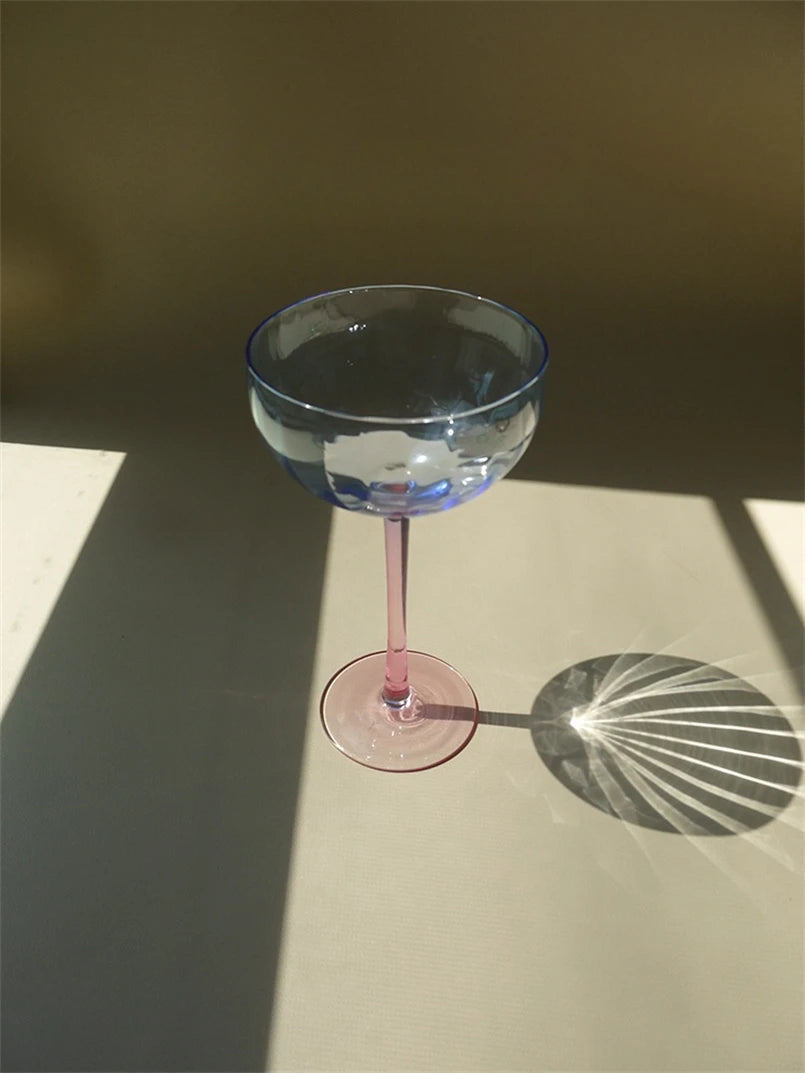 A vibrant collection of Ugo Wine Glasses displayed on a table, showcasing their fun and chic design. Each glass features a colored pastel bowl with a contrasting stem and a fluted shape. Ideal for entertaining, these glasses hold 11 fluid ounces and are perfect for mixing and matching. Designed for home décor enthusiasts, they add a playful yet elegant touch to any bar or dining setting.