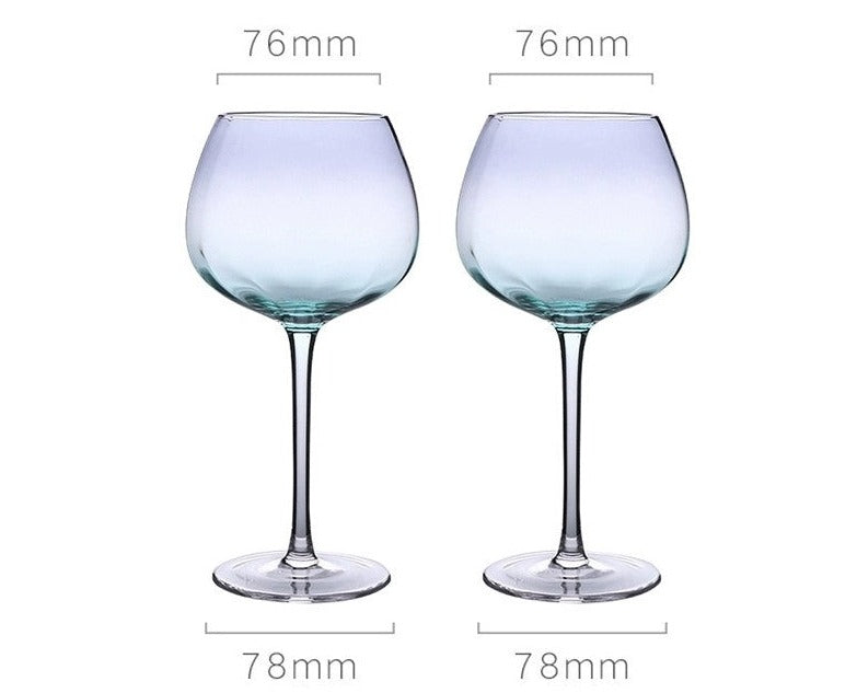 A collection of iridescent glassware from Domus Forge, featuring wine glasses, champagne coupes, decanters, and highball glasses in pastel gradient hues.