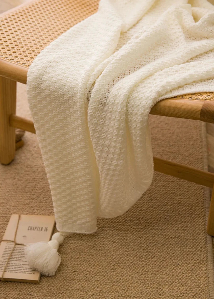 Image of the Soma Throw Blanket, featuring a cozy, soft fleece and cotton blend with a waffled texture. Available in various colorways and three sizes, this throw blanket has elegant tasseled corners and a knitted design, perfect for home décor enthusiasts looking to add comfort and style to their living space.