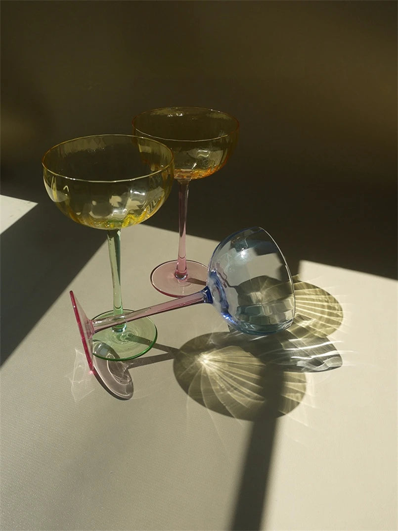 A vibrant collection of Ugo Wine Glasses displayed on a table, showcasing their fun and chic design. Each glass features a colored pastel bowl with a contrasting stem and a fluted shape. Ideal for entertaining, these glasses hold 11 fluid ounces and are perfect for mixing and matching. Designed for home décor enthusiasts, they add a playful yet elegant touch to any bar or dining setting.