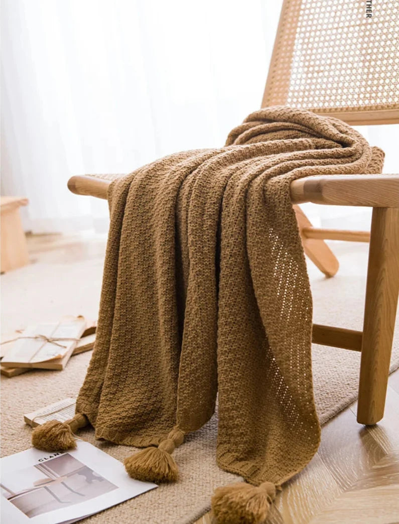 Image of the Soma Throw Blanket, featuring a cozy, soft fleece and cotton blend with a waffled texture. Available in various colorways and three sizes, this throw blanket has elegant tasseled corners and a knitted design, perfect for home décor enthusiasts looking to add comfort and style to their living space.