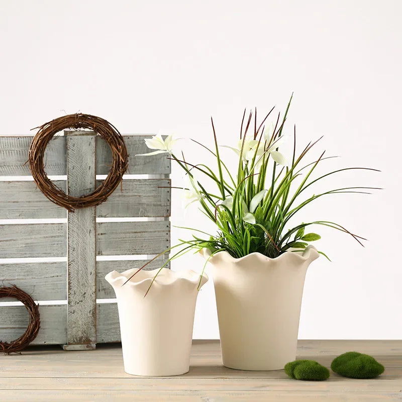 A ceramic planter with a wavy edge design, shown in a soft neutral color. The planter is available with or without a matching tray and comes in both small and large sizes, making it perfect for showcasing indoor greenery like succulents or ferns.