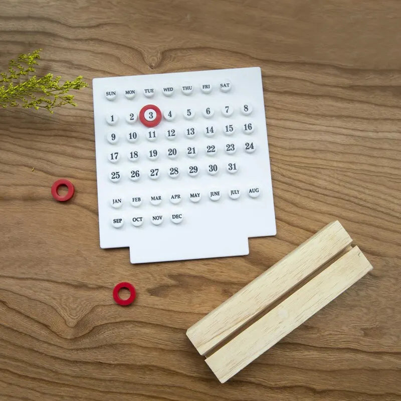 Image of the Callie Calendar, a compact, reusable calendar in black or white with a sleek acrylic design and a natural wooden stand. Features a red marker for highlighting important dates, perfect for organizing spaces like the kitchen or office with a touch of style.