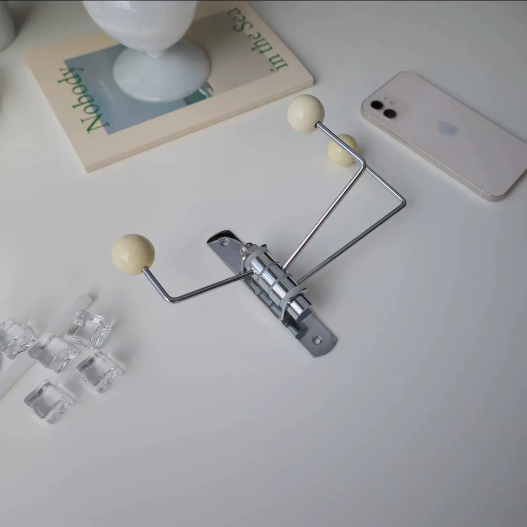 A silver wall-mounted rack with three hooks, each featuring bright wooden ball accents. The Randi Wall Rack has a modern yet vintage-inspired design, ideal for hanging towels or accessories in entryways, bathrooms, or bedrooms. Perfect for home decor enthusiasts seeking a stylish, space-saving storage solution.
