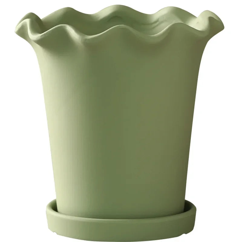 A ceramic planter with a wavy edge design, shown in a soft neutral color. The planter is available with or without a matching tray and comes in both small and large sizes, making it perfect for showcasing indoor greenery like succulents or ferns.