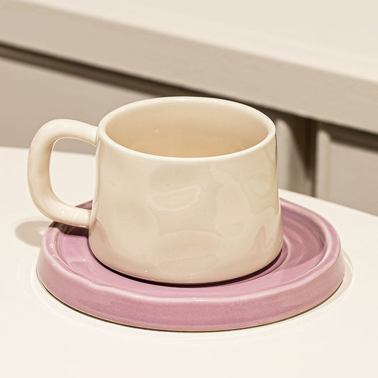 Organic-shaped cream mug & saucer set with orchid colorway, perfect for coffee & tea lovers.