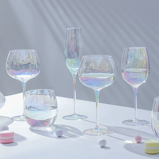  A collection of iridescent glassware from Domus Forge, featuring wine glasses, champagne coupes, decanters, and highball glasses in pastel gradient hues.