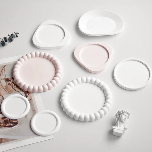 A collection of plaster trays from the Quinto Tray Collection, featuring various shapes and neutral colorways, suitable for use in different areas of the home.