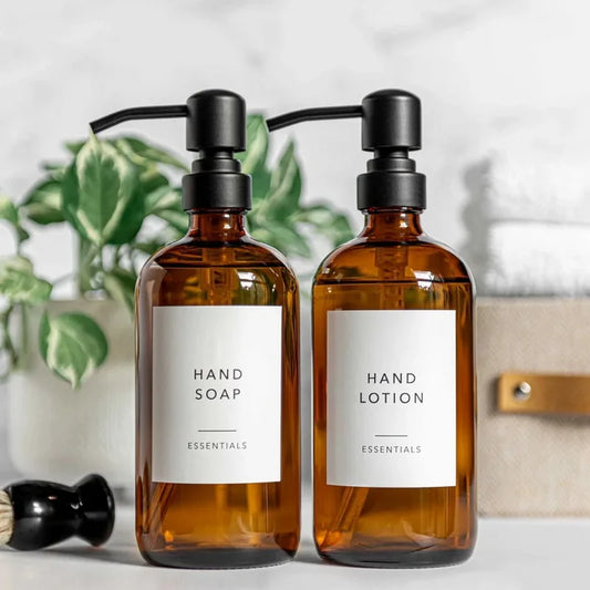 A set of two amber glass soap dispensers, each with a 16 oz capacity, featuring a choice of silver or black stainless steel pumps. Includes six printed labels for easy identification. Ideal for home décor enthusiasts, this reusable and refillable set adds a stylish touch to kitchens and bathrooms.