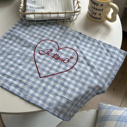 A checkered placemat available in blue or pink, featuring red "je t'aime" embroidery along one edge. Made of soft cotton gauze, the placemat has a vintage, French-inspired charm and measures 30 x 40 cm. Ideal for home decor enthusiasts adding a nostalgic, romantic touch to their dining table.