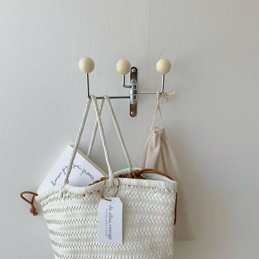 A silver wall-mounted rack with three hooks, each featuring bright wooden ball accents. The Randi Wall Rack has a modern yet vintage-inspired design, ideal for hanging towels or accessories in entryways, bathrooms, or bedrooms. Perfect for home decor enthusiasts seeking a stylish, space-saving storage solution.